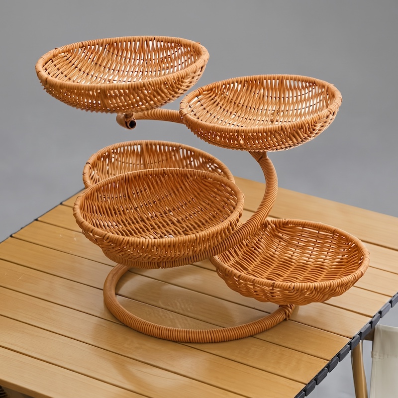 A 3/4 view of the assembled multi-layer spiral rattan fruit platter storage basket, featuring four empty woven bowls, sitting on a slatted light wood table against a neutral background.