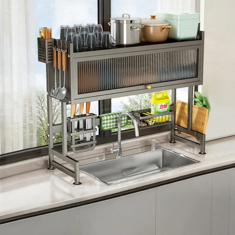 A three-quarter angled view of a black stainless steel Dish Rack Above Sink 3 Levels, placed over a large sink on a light-colored countertop, fully stocked with dishes, pots, and a knife block against a window.