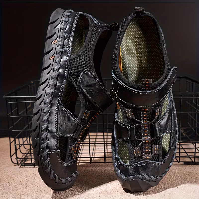 All-Terrain Casual Sports Sandals: Solid Color, Slip-Resistant Rubber Sole & Breathable Fiber Upper 3 A product photograph displaying a pair of men's black color Casual Sports Sandals Solid Color standing upright against a dark background with a wire mesh basket. The sandals feature a closed-toe design, mesh paneling, leather straps, and rugged soles.