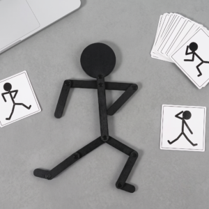 A black wooden figure from the Wooden Puzzle Versatile game posed on a grey desk with matching action cards.
