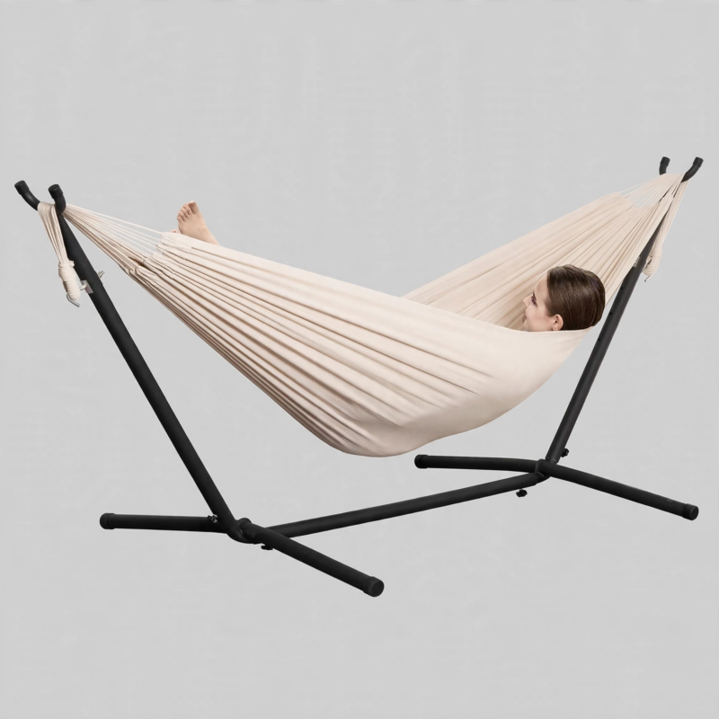 Studio front view of a person lying comfortably in a beige Double Hammock with Stand Included against a plain background.