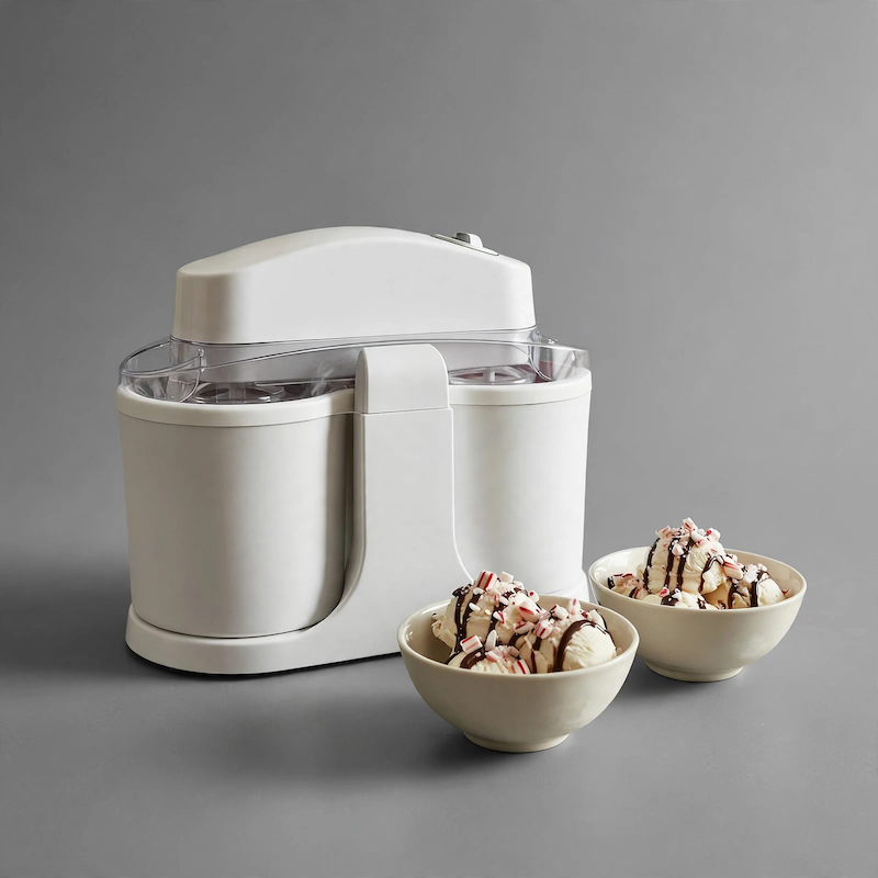 Home Ice Cream, Detachable Design for Easy Cleaning, Perfect for Making Homemade Ice Cream, Smoothies And Frozen Yogurt, 1QT, Party, Summer Essentials, Halloween And Christmas Gifts Suitable for Giving 7 Front view of an ivory white Home Ice Cream machine displayed on a gray surface alongside two bowls of ice cream drizzled with chocolate and candy toppings.