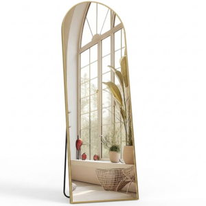 Front view of a golden color Arched Full Length Mirror with Free Standing frame isolated on a white background reflecting a large bright window and green plants