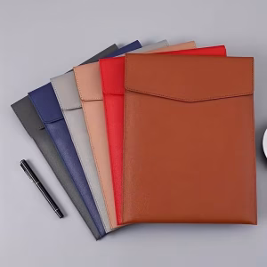 A professional product photograph showcasing the multi colors holder designed for storing files, presented on a gray linen surface against the softly blurred background of a large window with a potted green plant and soft curtains. The visualization details the unique, vibrant construction of the holder, which features a multi-color patchwork of premium perforated Napa leather panels, including segments of cobalt blue, scarlet red, emerald green, canary yellow, and sunburst orange, all precisely joined with sophisticated complex pleated stitching. The intricate material fidelity emphasizes the 'Multi Colors Holder Designed for Storing Files' text, which is clearly embossed in a refined gold script on the front u-shaped pocket. Natural, diffused cool daylight highlights the micro-perforations and complex pleating logic of the file holder, defining it as a paramount standard of 'Aesthetic Purity' and 'Structural Sustenance' within the workspace context. On the gray linen surface next to the holder, the single matte black glass bottle of 'Jelly Ice Nude' AL14 polish (Shade: AL14) and the gradient swatch card are in sharp, high-definition focus. The text on the AL14 card is sharply clear. All details within the original hand pose are preserved and rendered with sharp clarity.