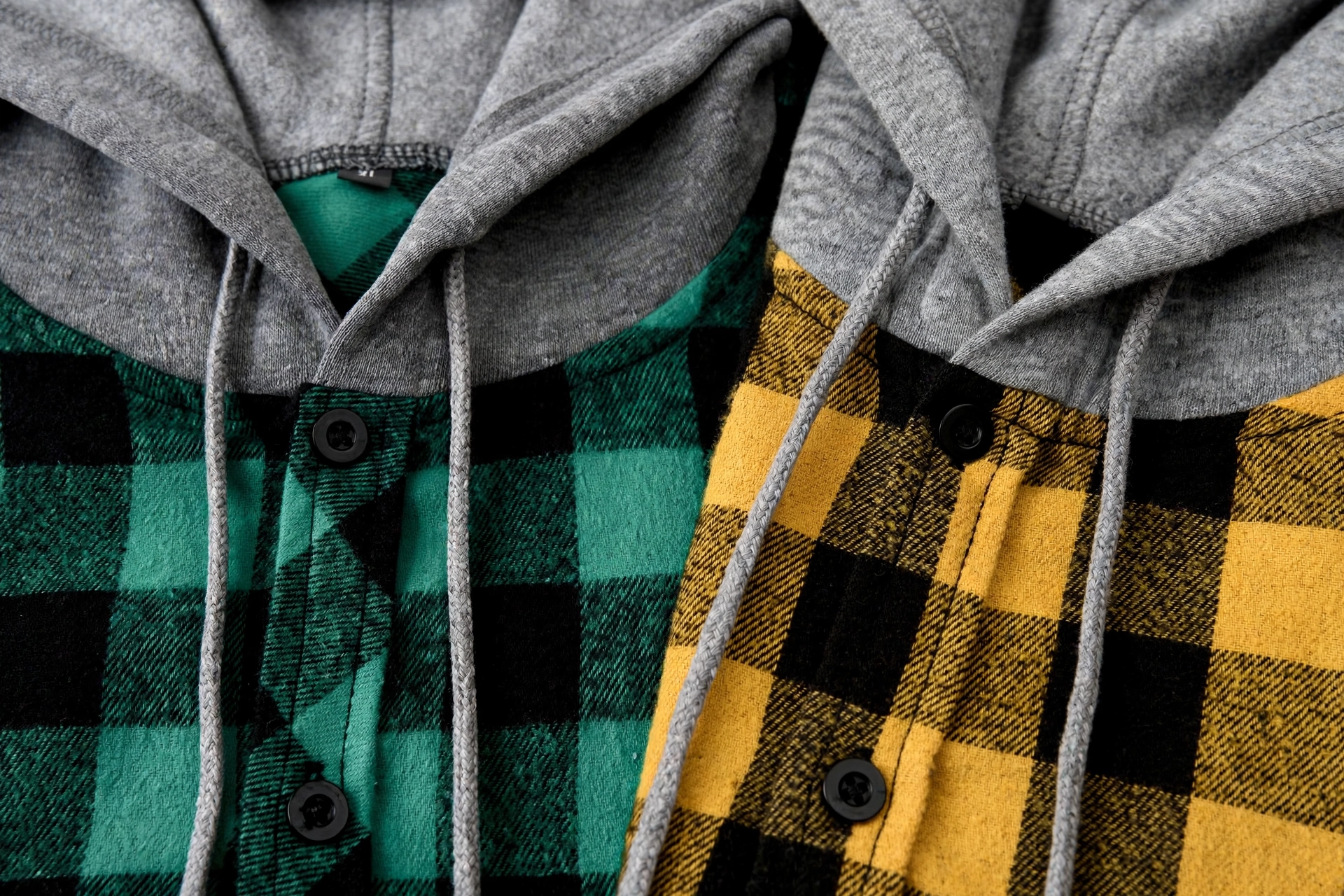 2pcs Men's New York Fashion Trendy Plaid Shirt Hoodie, Plaid Pullover Sweatshirt Flannel Hoodie 38 Close-up macro view of the green and yellow flannel fabrics, buttons, and gray hoods of two fashion trendy plaid shirt hoodies.