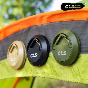 Three circular CLS Magnetic Camping Hooks, in tan, black, and olive green, are shown attached to the grey seam fabric of a camping tent. A folding stainless steel loop is visible on each. The CLS Outdoor Camping logo is in the upper right.