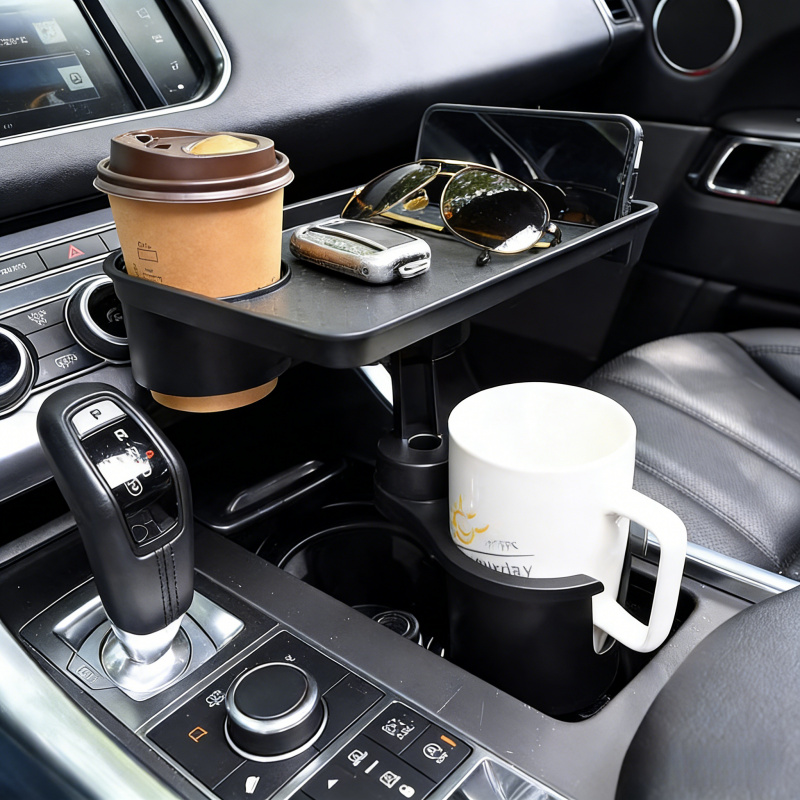 Operational Infrastructure Node: Car Cup Holder Expansion Tray with 40lb Load Capacity and 360° Rotating Mechanical Base for Superior Cabin Utility 6 A professional high-definition lifestyle photograph of the Car Cup Holder Expansion Tray integrated into a luxury vehicle's center console. The matte black hardware is securely anchored in the primary cup holder, supporting a large white ceramic mug with a handle. The elevated expansion tray is positioned above the gear shifter, holding a disposable coffee cup in its secondary well, alongside a pair of aviator sunglasses, a vehicle key fob, and a smartphone. The vehicle interior features high-compliance leather seating and a detailed dashboard interface. The focus is sharp on the structural stability of the tray and its capacity to organize multiple personal assets in a unified, accessible workspace.