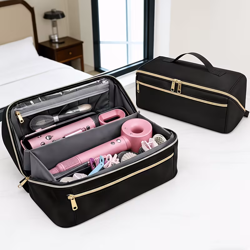3-in-1 Clutch Bag Hot Hair Tools Travel Bag – Large Capacity Wide-Open Hair Accessory Case & Professional Heat-Safe Styling Mat 1 Two black color clutch bag hot hair tools travel bags are resting on a white desk in a bedroom setting. One travel bag is open, showing a neat interior with pink hair tools like a blow dryer and flat iron, plus various hair accessories and makeup brushes. The other black color clutch bag hot hair tools travel bag is closed, sitting behind it to display its sleek design and gold zipper accents. A bed and nightstand are visible in the background.