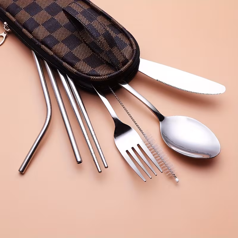 reliable Unyielding Travel Utensils Reusable Silverware Set: Professional-Grade Stainless Steel Cutlery in a Weatherproof Armor Case 12 he brown plaid sliver color Travel Utensils Reusable Silverware Set displayed on a light gray concrete surface in an outdoor garden setting. On the right, a rugged zippered carrying bag features a sophisticated brown plaid pattern with integrated brown mesh venting panels and a tactical handle loop.