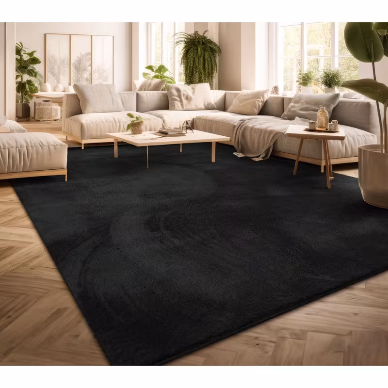 exclusive Modern Living Room Rug – Washable Short Pile Area Rug | Stain-Resistant & Non-Slip Premium Polyester 2 A large deep black modern living room rug laid across a light herringbone hardwood floor beneath a contemporary cream colored sectional sofa and minimalist wooden coffee tables in a bright sunlit room filled with houseplants