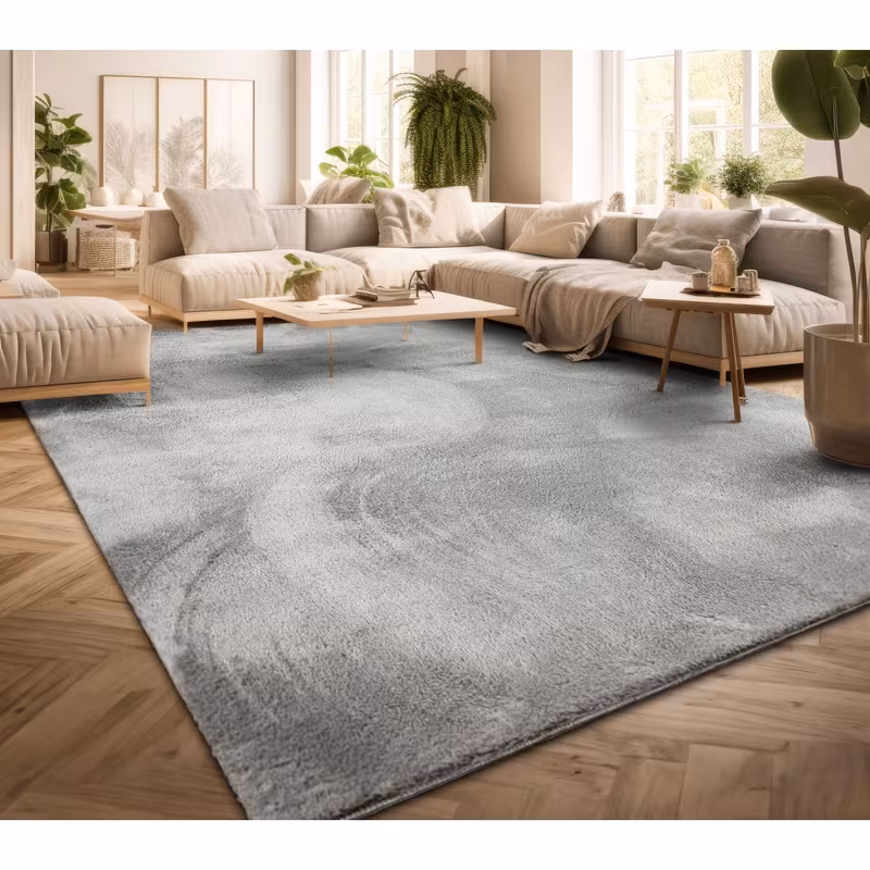 exclusive Modern Living Room Rug – Washable Short Pile Area Rug | Stain-Resistant & Non-Slip Premium Polyester 8 A large, silvery gray modern living room rug laid across a light herringbone hardwood floor, featuring a neutral cream modular sectional sofa and minimalist wooden coffee tables in a bright, sunlit room with indoor plants.