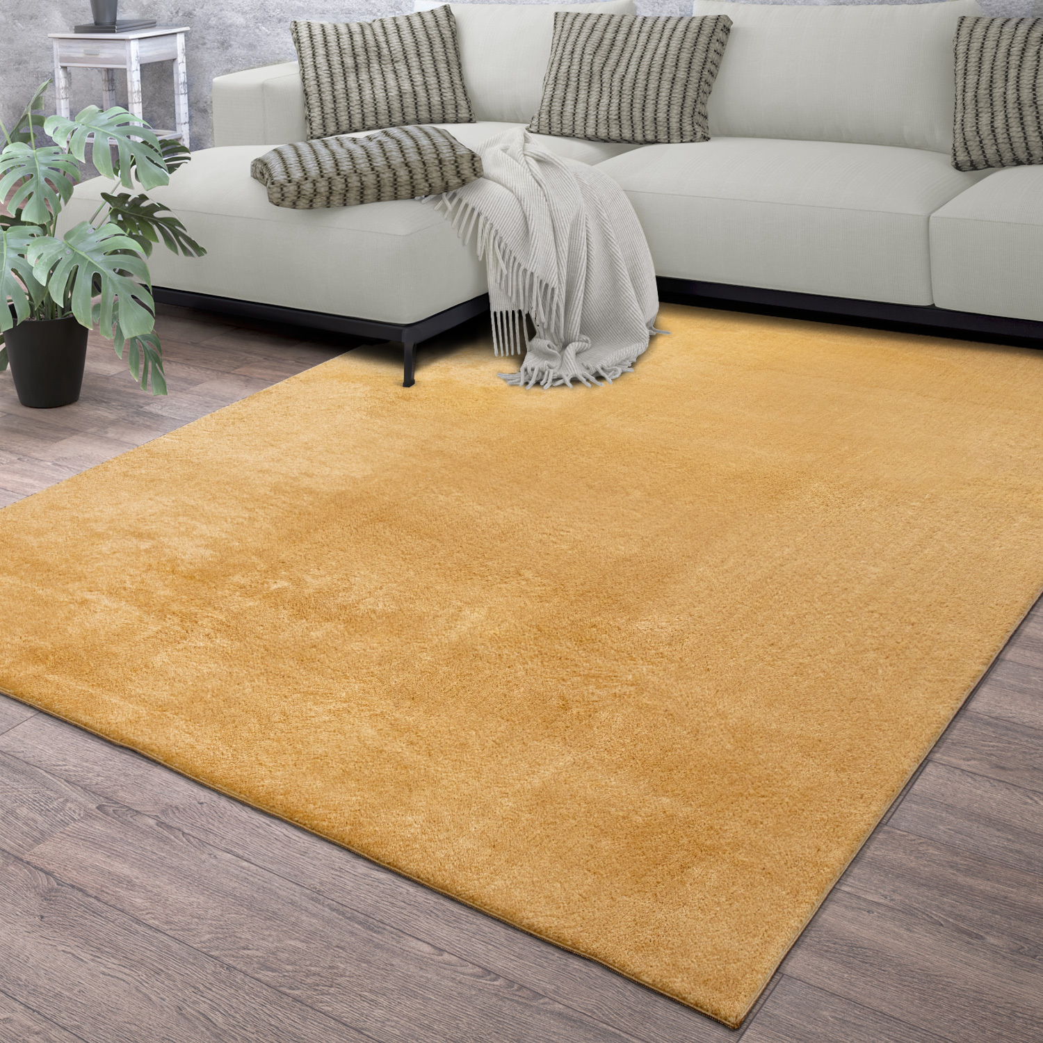 exclusive Modern Living Room Rug – Washable Short Pile Area Rug | Stain-Resistant & Non-Slip Premium Polyester 10 A large golden yellow modern living room rug spread across a dark wood floor beneath a cream sectional sofa with textured gray pillows and a potted green monstera plant